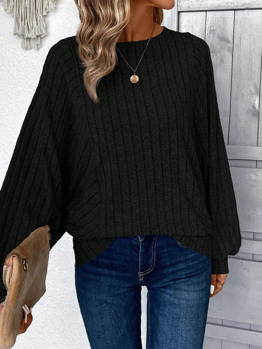 Woman wearing a black ribbed knit sweater with batwing sleeves and blue jeans, holding a tan clutch.