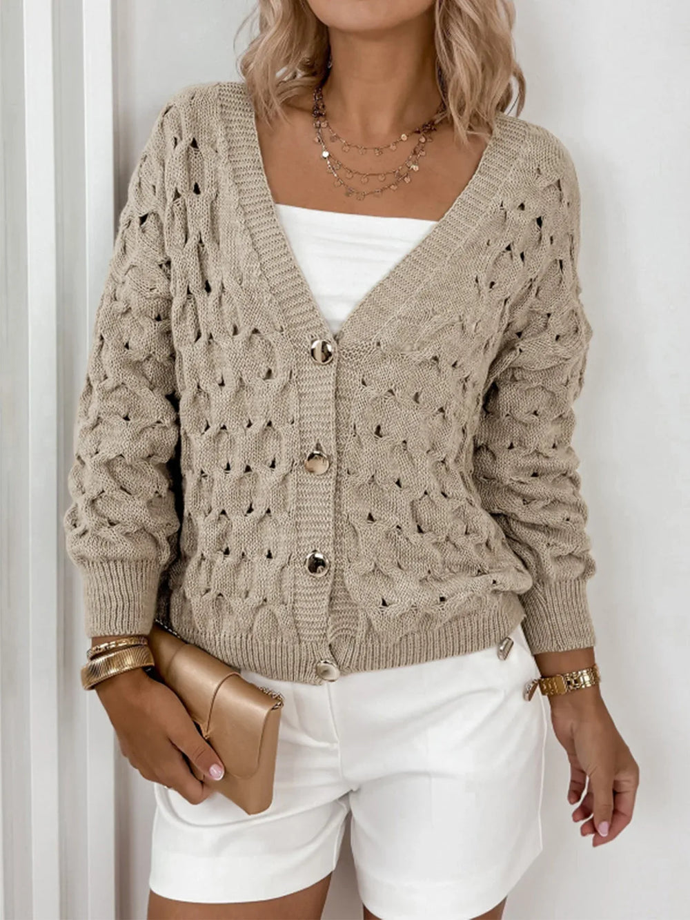 Woman's torso showing a beige open-knit V-neck cardigan with gold buttons, a white tube top, and white shorts.