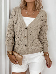 Woman's torso showing a beige open-knit V-neck cardigan with gold buttons, a white tube top, and white shorts.