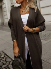 Close-up of a woman wearing a long brown knit cardigan with a white top and jewelry.