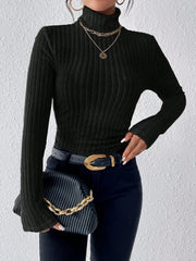 Woman wearing a black ribbed turtleneck sweater, black jeans, a black belt with a gold buckle, and holding a black clutch with a gold chain.
