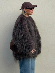 Woman in a brown shaggy faux fur jacket, blue jeans, and a brown baseball cap, viewed from the side.