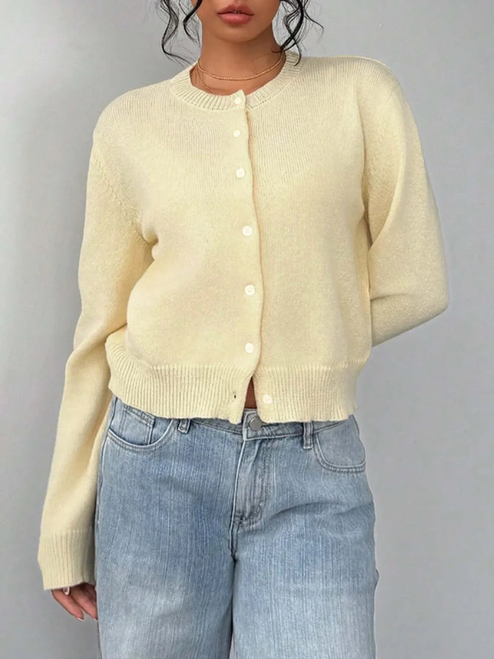 Front view of a model wearing a light yellow knit cropped cardigan buttoned up, with a white camisole visible, and light-wash wide-leg jeans.