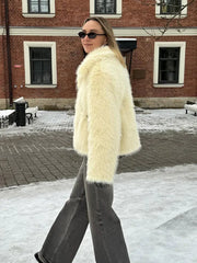 Woman in a cream faux fur jacket and grey jeans walking in the snow.