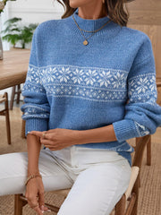 Woman sitting and wearing a blue knit sweater with a white Fair Isle snowflake and reindeer pattern, white pants.