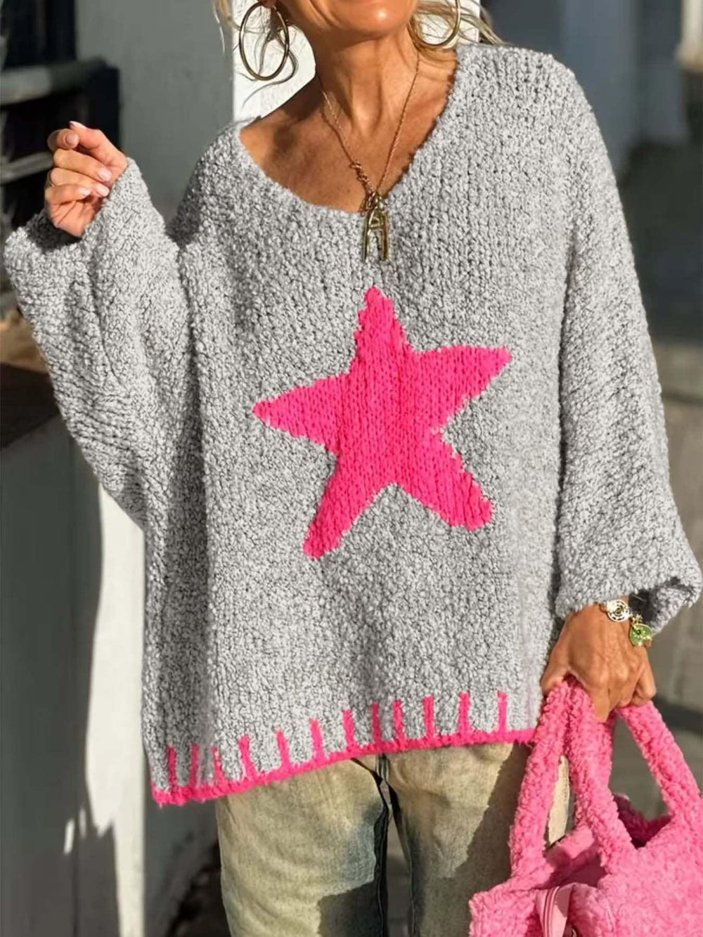 Woman holding a pink bag while wearing a grey knitted sweater with a pink star graphic