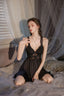 Woman in black lace-trimmed satin chemise and matching robe, kneeling on a bed.
