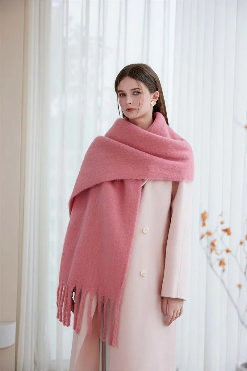 Woman wearing a pink oversized mohair blend scarf draped over a light pink coat.
