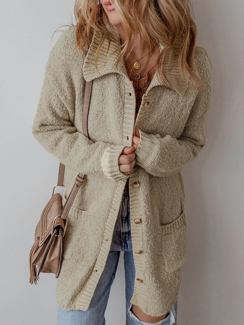 Woman adjusting the buttons of a long beige knit cardigan