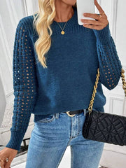 Woman wearing a blue knit sweater with cutout sleeves, blue jeans, and holding a black quilted handbag.