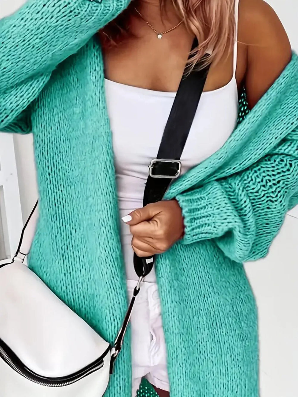 Close-up of a woman wearing an aqua knit cardigan over a white tank top, with a white crossbody bag.