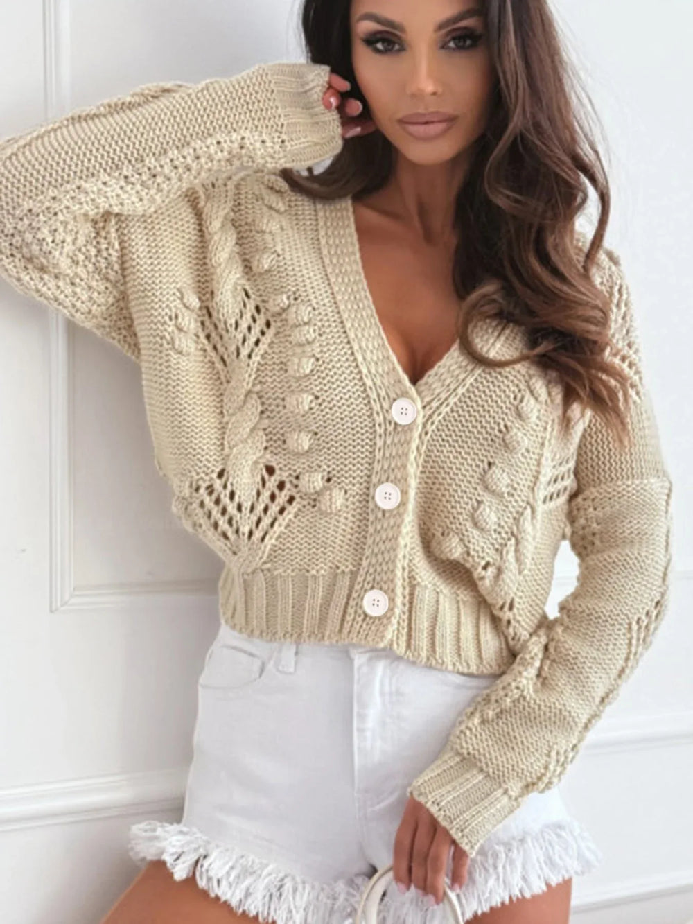 Close-up of a cream-colored, open-knit, cropped cardigan with a V-neck and button-up front.