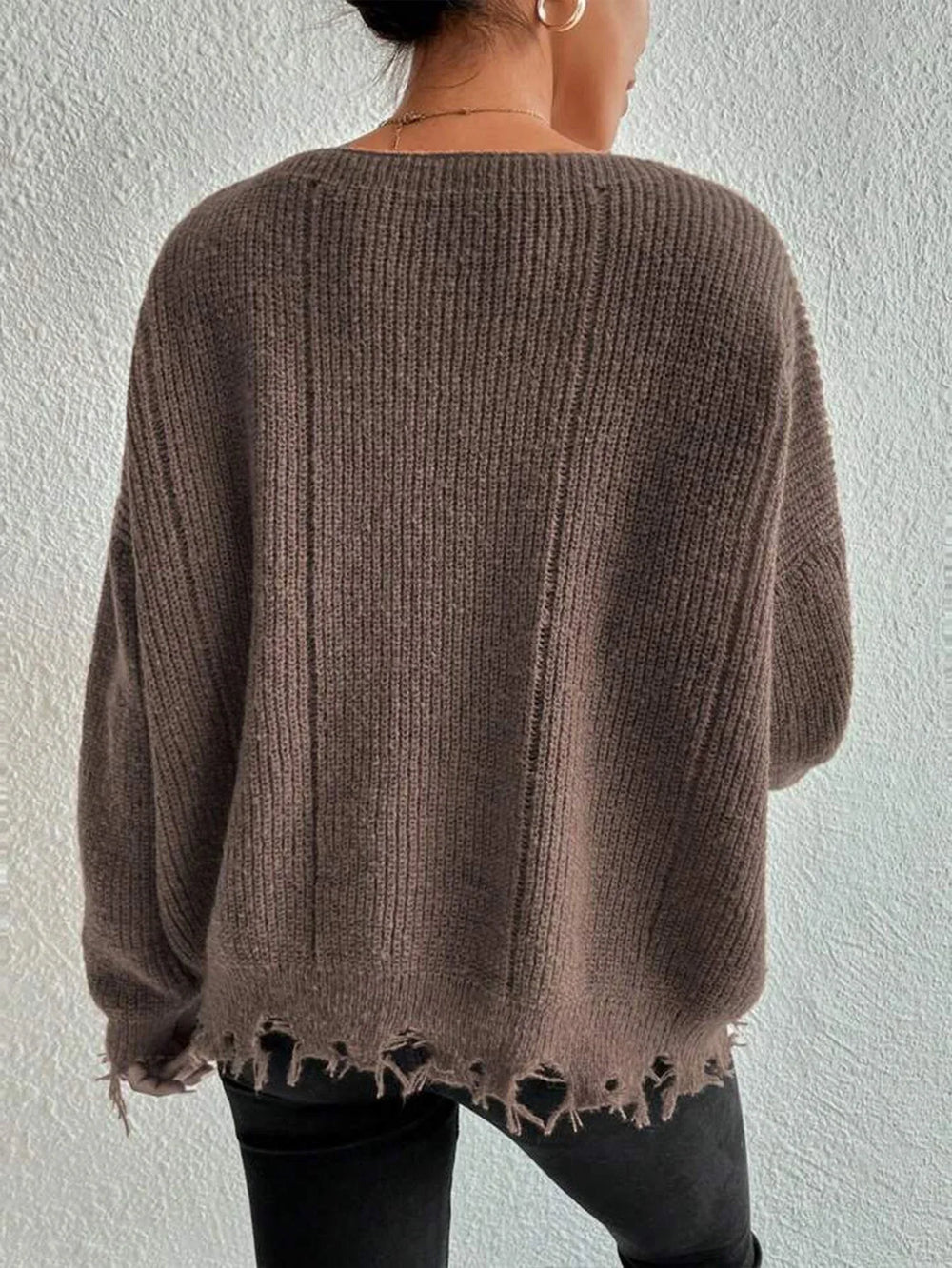 Back view of a woman wearing a brown oversized distressed knit sweater with black pants