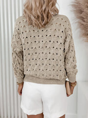 Back view of a woman wearing a beige open-knit V-neck cardigan with gold buttons and white shorts.