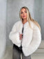 Woman wearing a white fluffy faux fur cropped jacket with dark wash jeans, looking to the side.