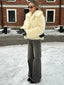 Woman wearing a cream faux fur jacket and grey wide-leg jeans standing in the snow.