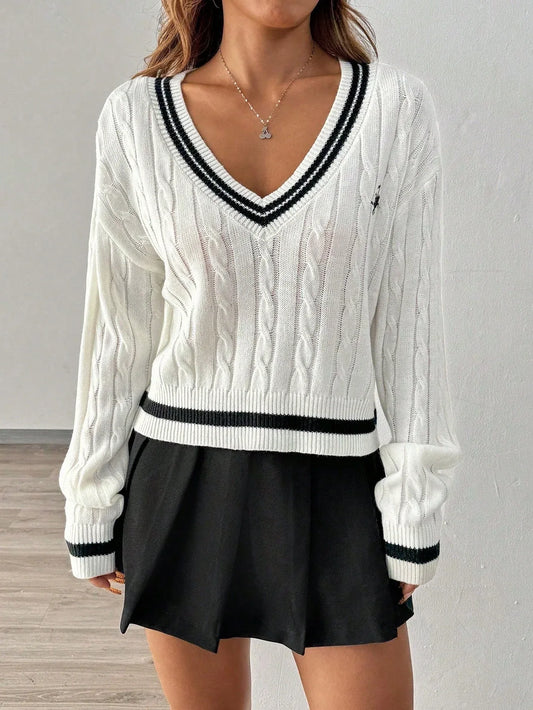 Woman wearing a white cable knit cropped sweater with black trim and a black pleated skirt, front view.