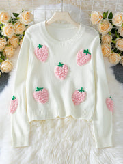 White cropped knit sweater with multiple pink strawberry appliques, displayed on a hanger with a floral background.