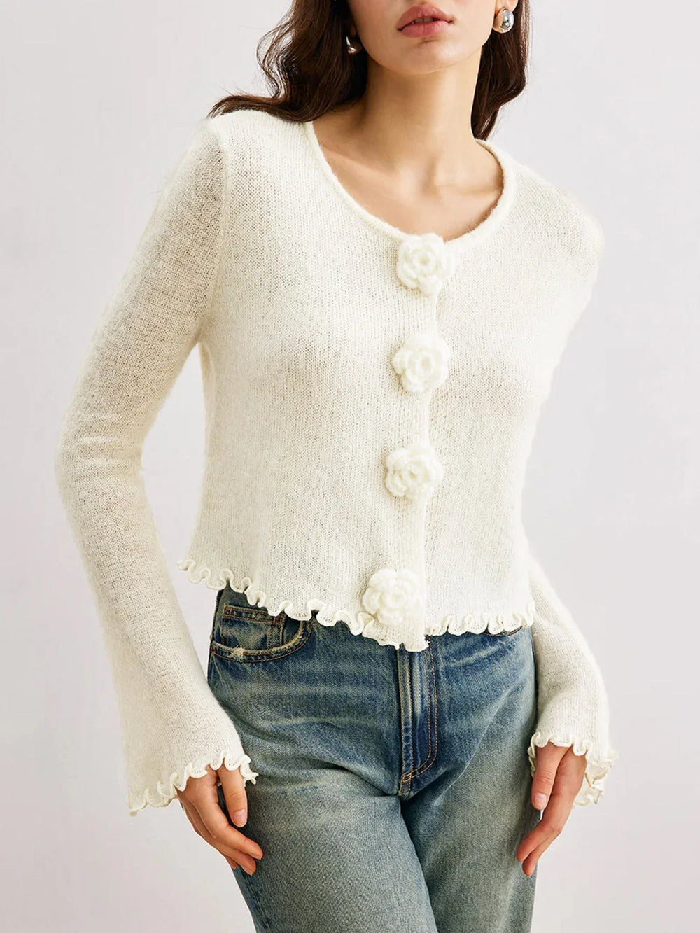 Woman in a white knit cardigan with bell sleeves and ruffled cuffs.