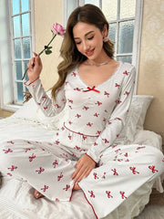woman wearing white and red bow print pajama set sitting on a bed holding a rose