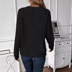 Back view of a woman wearing a black ribbed V-neck long-sleeve sweater with dark wash jeans.