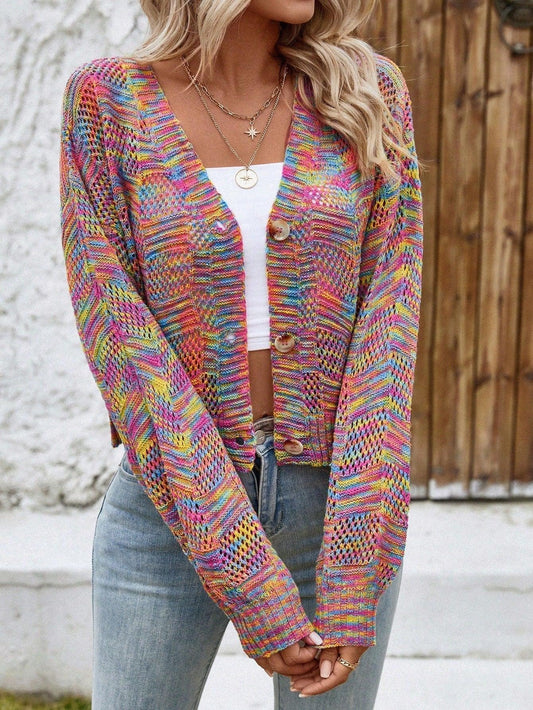 Woman wearing a multicolor rainbow knit cropped cardigan with a white top and blue jeans, standing outdoors.