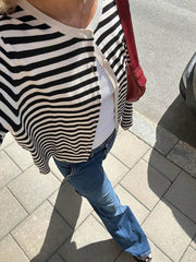 Top-down view of a woman's outfit featuring a black and white striped cardigan, white tank top, and blue jeans.