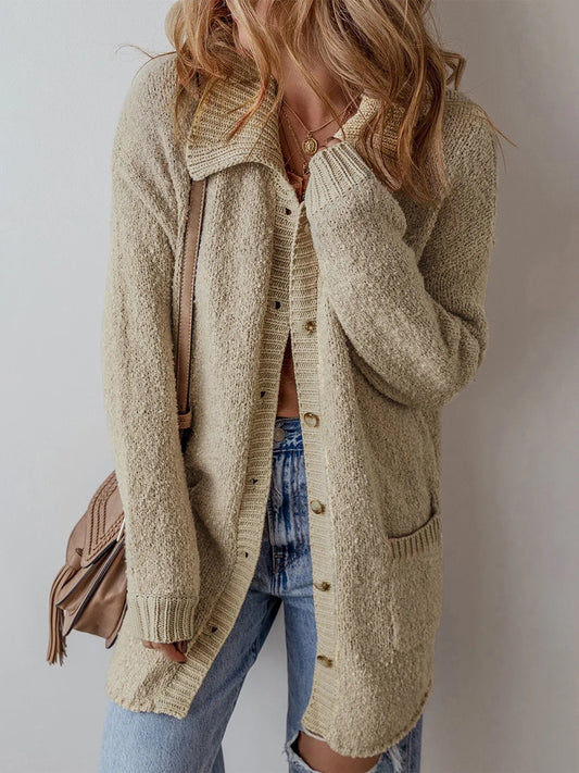 Woman wearing a long beige knit cardigan open with a brown top and blue jeans, carrying a brown crossbody bag
