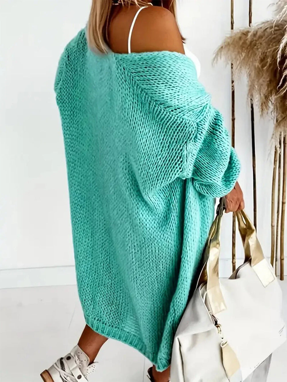 Rear view of a woman wearing a longline aqua knit cardigan, with the cardigan draped off one shoulder.