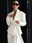 Woman wearing a white oversized blazer with wide lapels and a belted waist, paired with high-waisted pleated trousers and sunglasses.