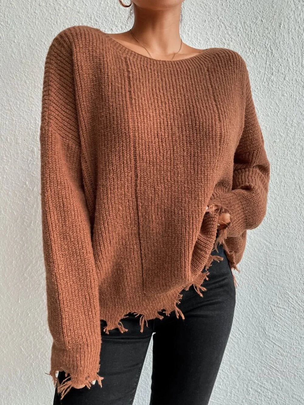 Woman wearing a rust-colored oversized distressed knit sweater with black pants and a necklace