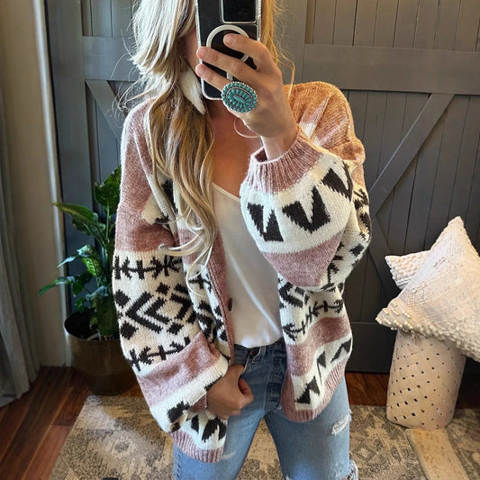 woman wearing a pink and black geometric print knit cardigan with a white tank top and blue jeans