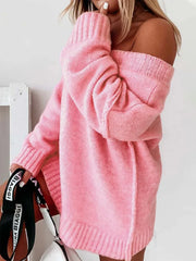 Woman in a pink oversized V-neck knit sweater with an off-the-shoulder design, holding a black and white bag.