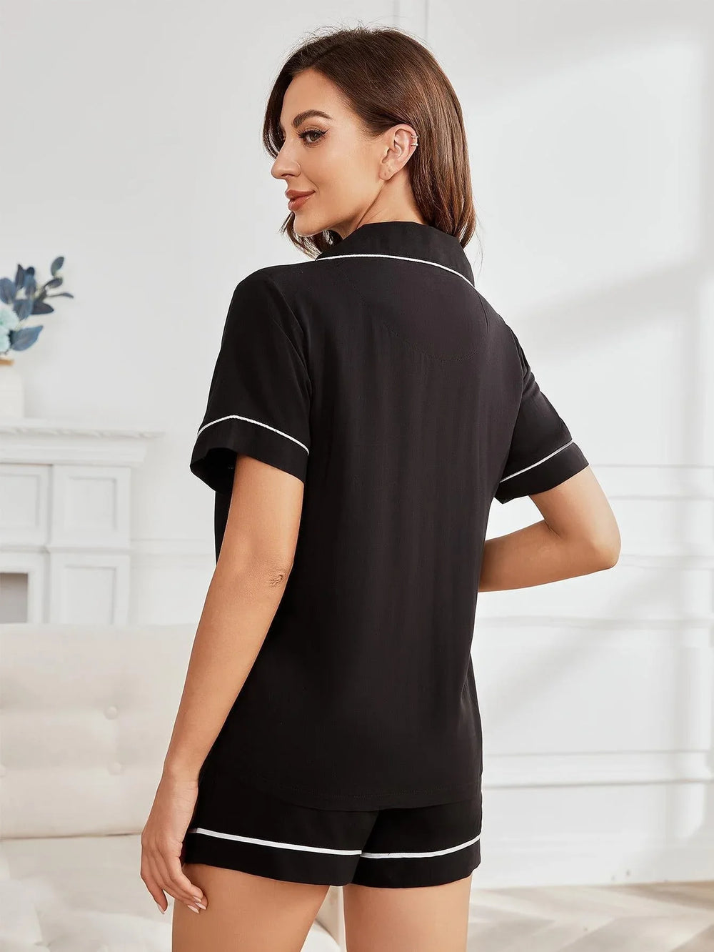 Woman from behind wearing a black short-sleeve pajama top with white piping.