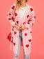 Woman wearing a pink longline cardigan with red hearts, paired with a white crop top and light wash jeans.