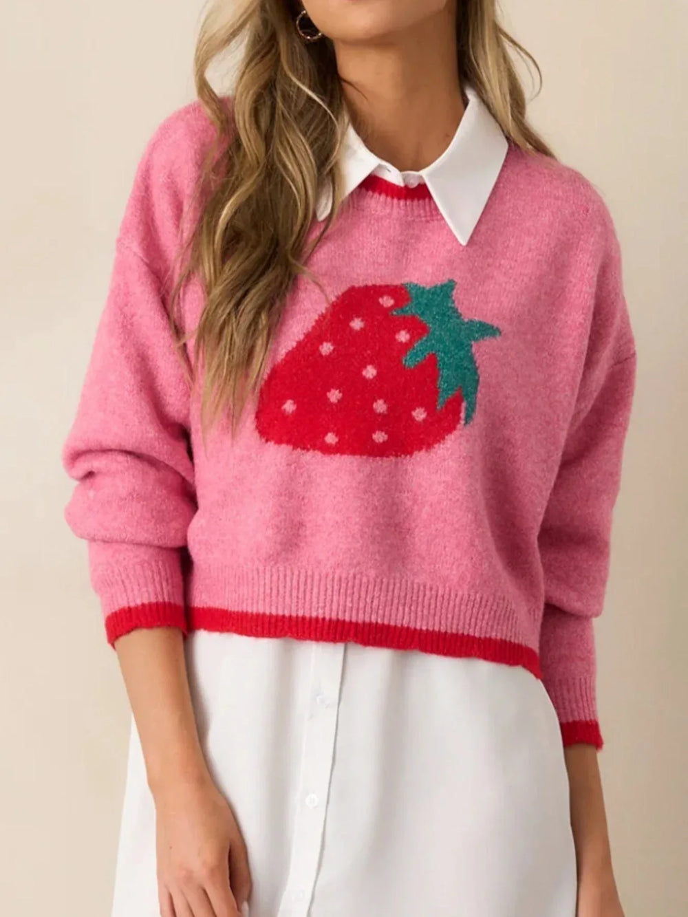 Woman wearing a pink cropped sweater with a strawberry graphic layered over a white shirt.