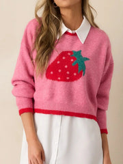 Woman wearing a pink cropped sweater with a strawberry graphic layered over a white shirt.