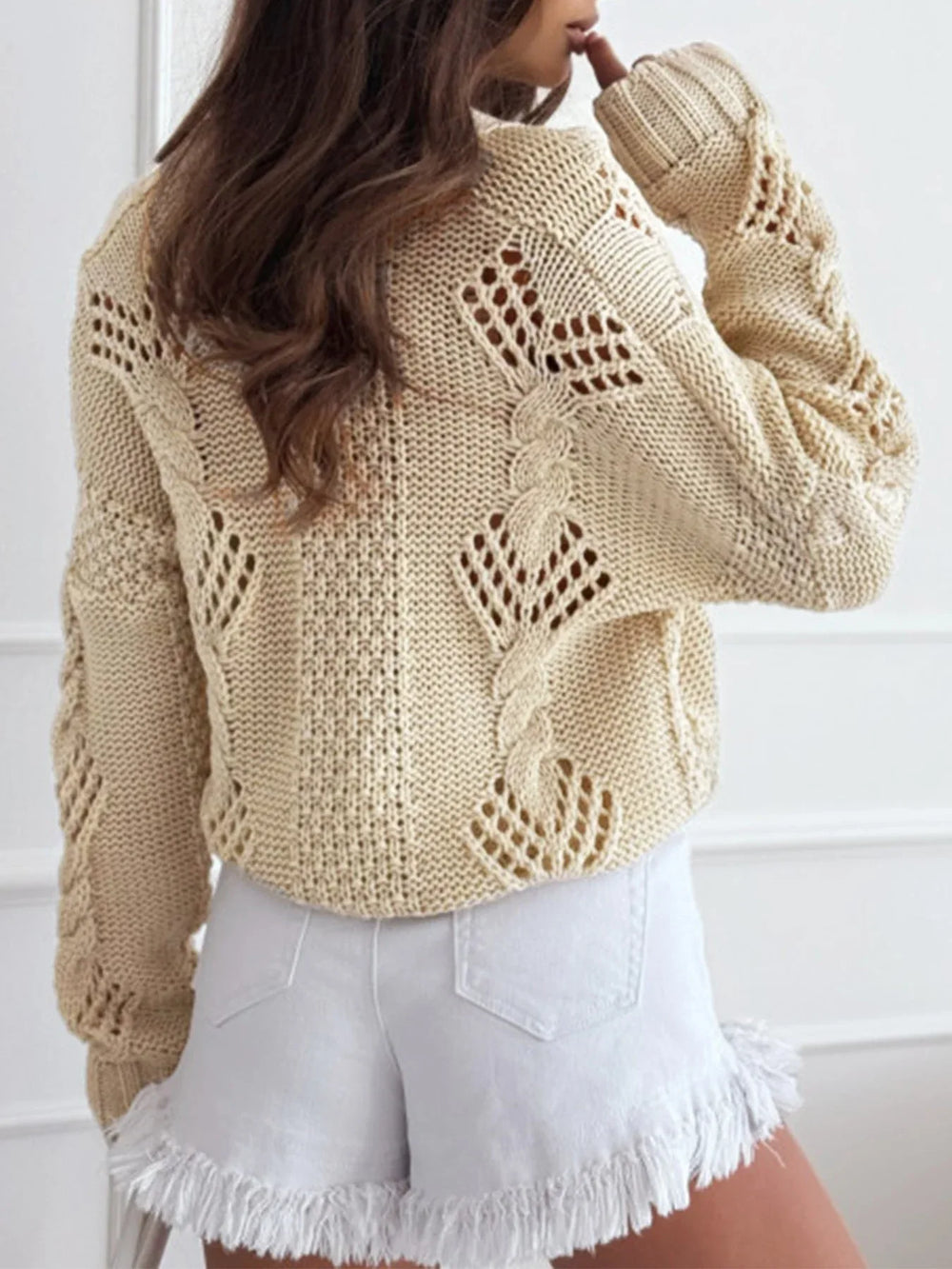 Back view of a cream-colored, open-knit, cropped cardigan with a V-neck and button-up front.