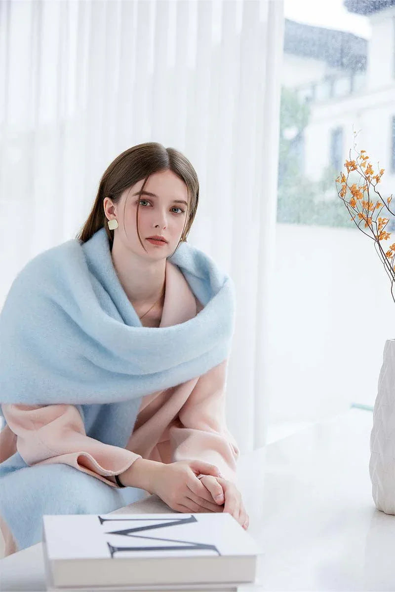 Woman wearing a light blue oversized mohair blend scarf draped over a pink coat.