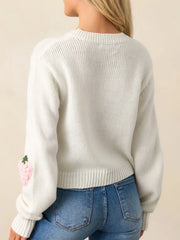 Back view of a white cropped knit sweater with a single pink strawberry applique on the sleeve, worn with blue denim jeans.
