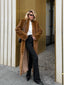 Woman wearing a long brown faux fur coat and black pants.