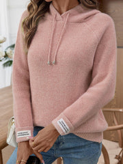 Close-up of a woman wearing a pink knit hoodie and blue jeans, showing the sleeve detail.