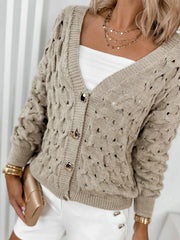 Close-up of the front of a beige open-knit V-neck cardigan with gold buttons, worn by a woman.