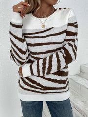 Woman posing with arms crossed, wearing a white and brown striped zebra print knit sweater and blue jeans.