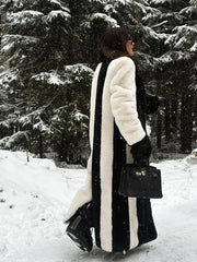 Rear view of a woman in a striking black and white vertical striped faux fur coat, walking in a snow-covered forest.