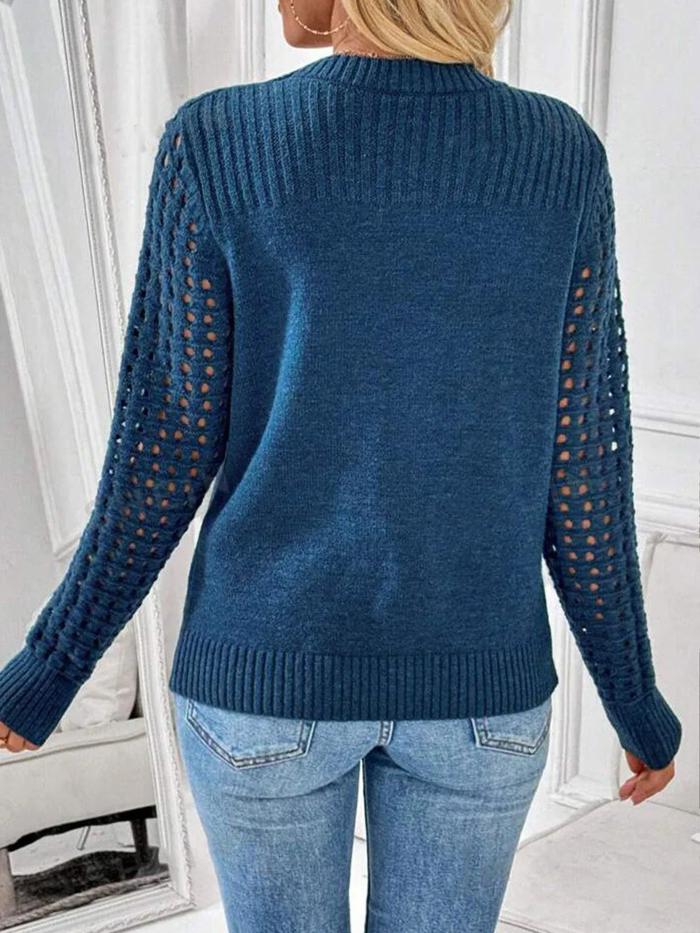 Back view of a woman wearing a blue knit sweater with cutout sleeves and blue jeans.