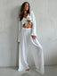 Woman wearing a white sheer knit crop top and wide-leg pants, standing against a wall.