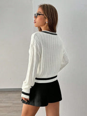 Woman wearing a white cable knit cropped sweater with black trim and a black pleated skirt, back view.