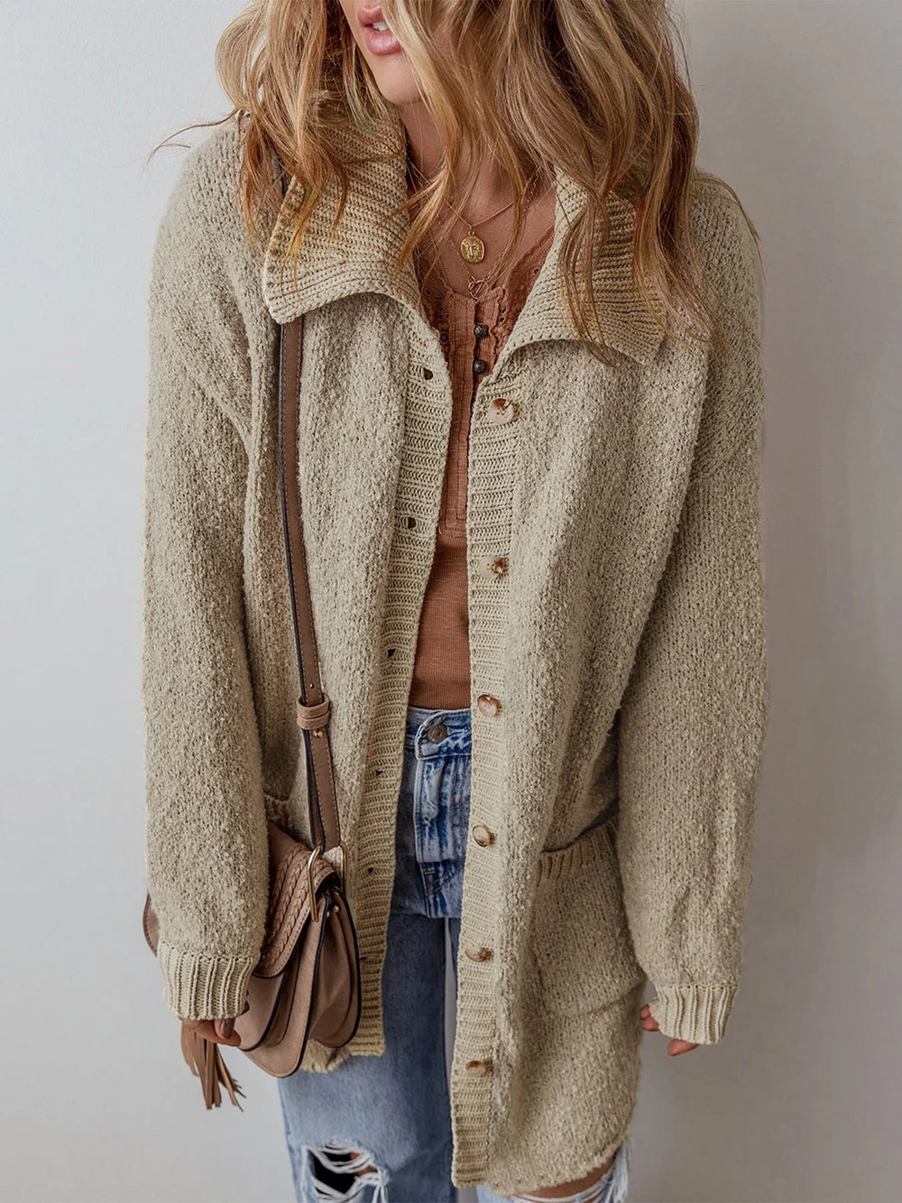 Woman wearing a long beige knit cardigan over a brown henley top and blue jeans