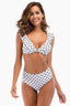 Woman smiling in a white and black polka dot bikini with ruffled trim and high-waisted bottoms.